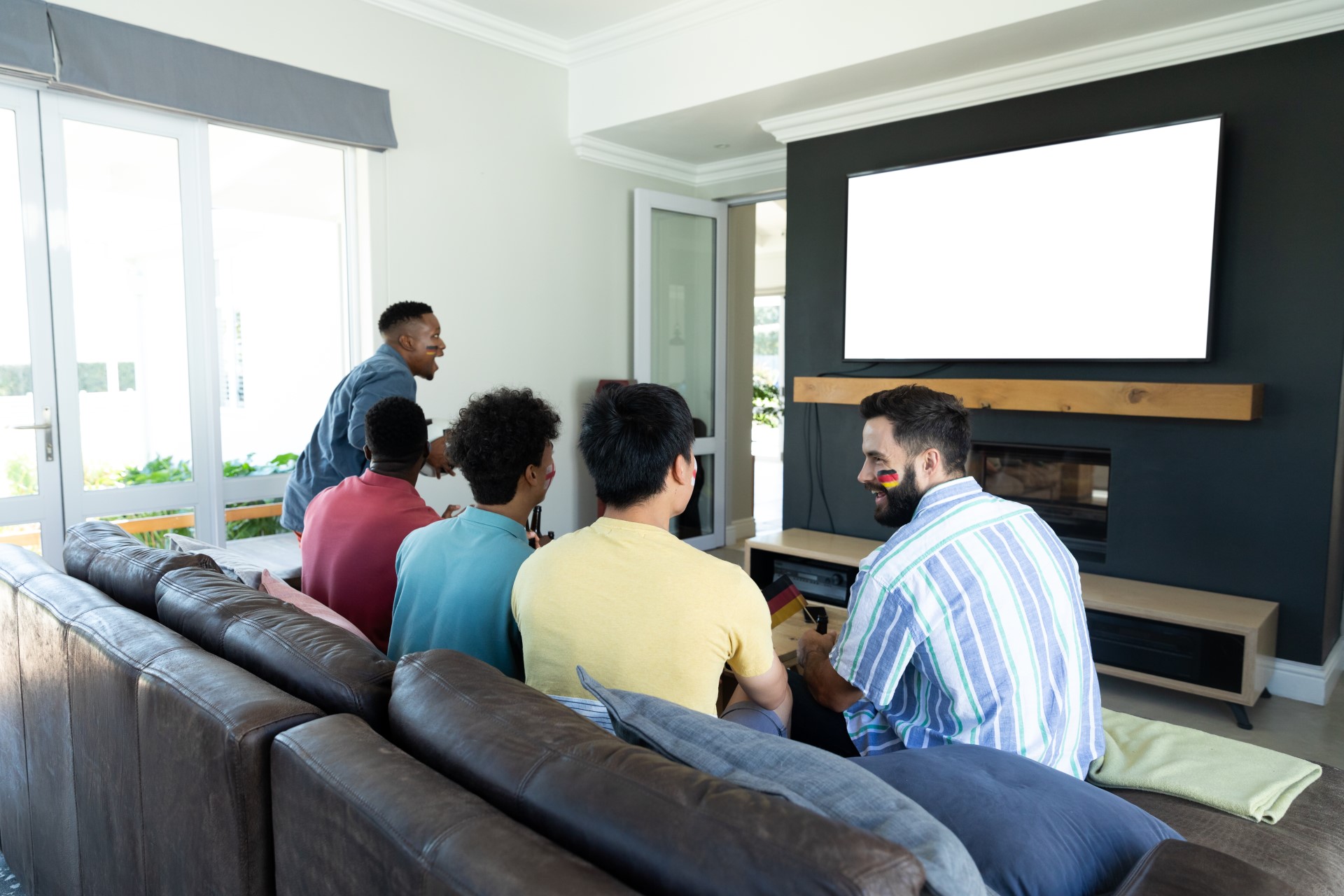 A group of men sit around a TV in the living room having fun.