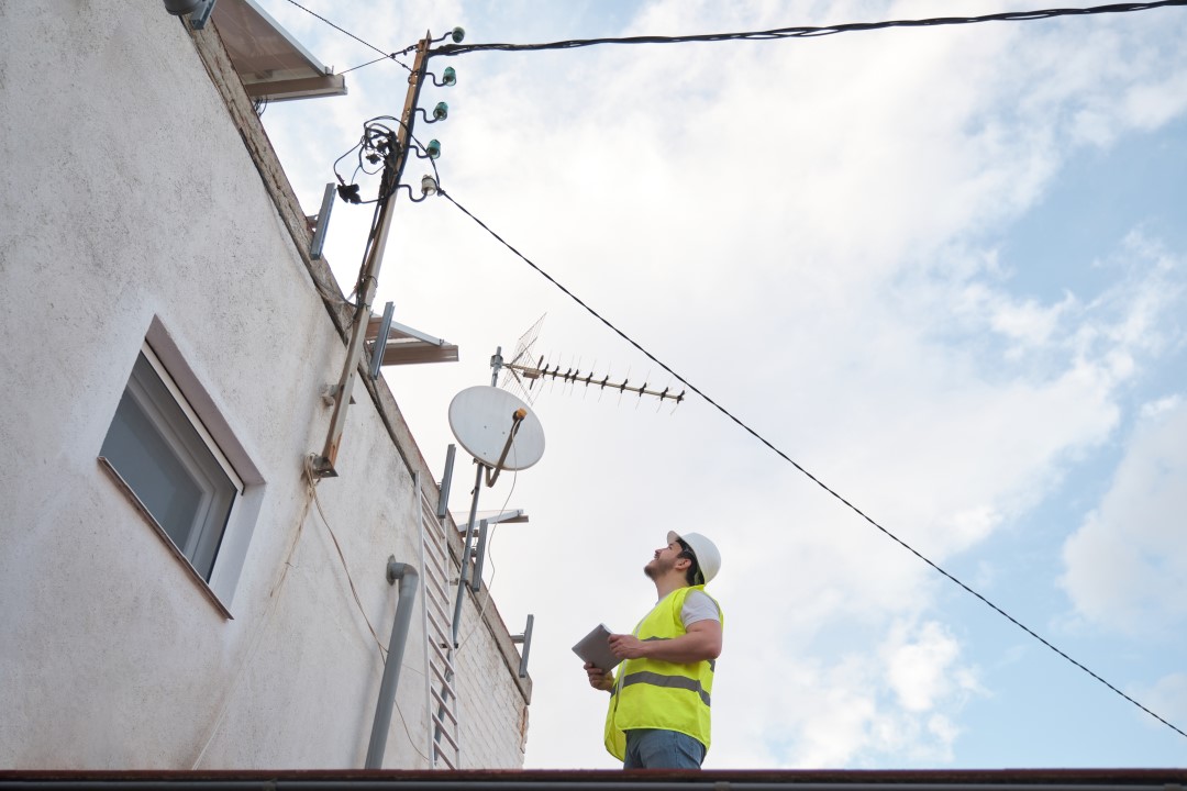 A technician looking up at the finished installation of an antenna on the roof of a building.